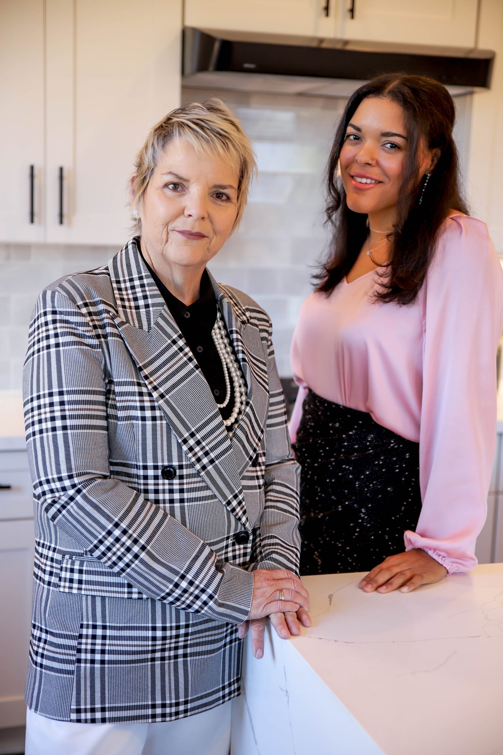 Two women standing in white kitchen leaning on kitchen island.